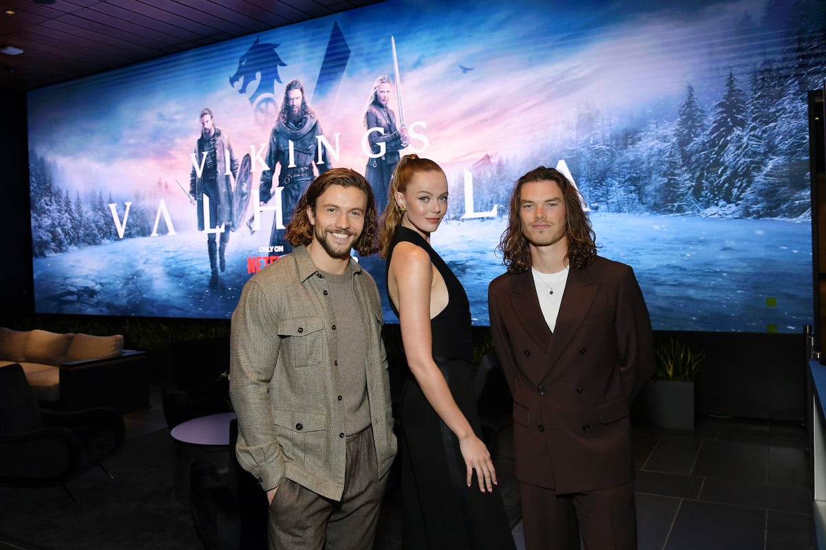 Leo Suter, Frida Gustavsson and Sam Corlett pose in front of a screen with the "Vikings: Valhalla" season 2 key image.