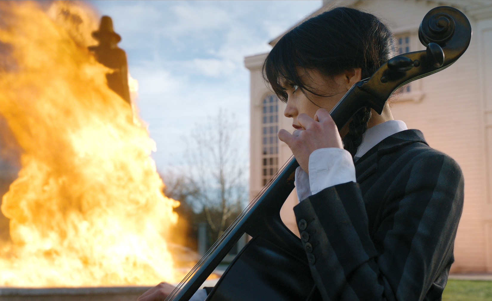 Jenna Ortega in 'Wednesday' for our article about when season 2 could premiere on Netflix. She's playing the cello and there's a fire behind her.