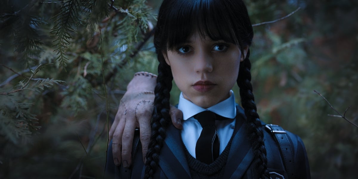 Jenna Ortega as Wednesday Addams with Thing the hand on her shoulder.