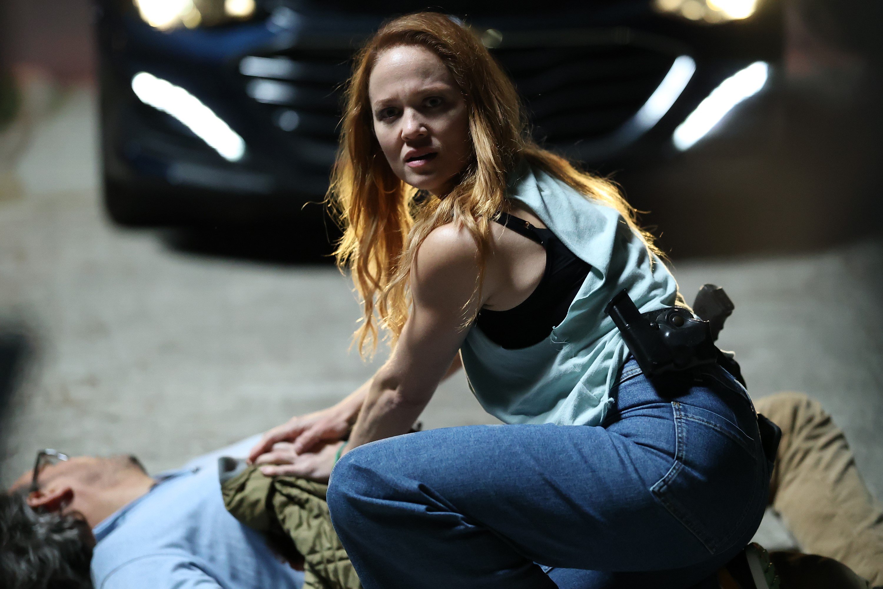 Erika Christensen, in character as Angie Polaski in 'Will Trent' Season 1 Episode 2, wears a light gray tank top over a black bra and jeans as she tends to a gunshot victim.