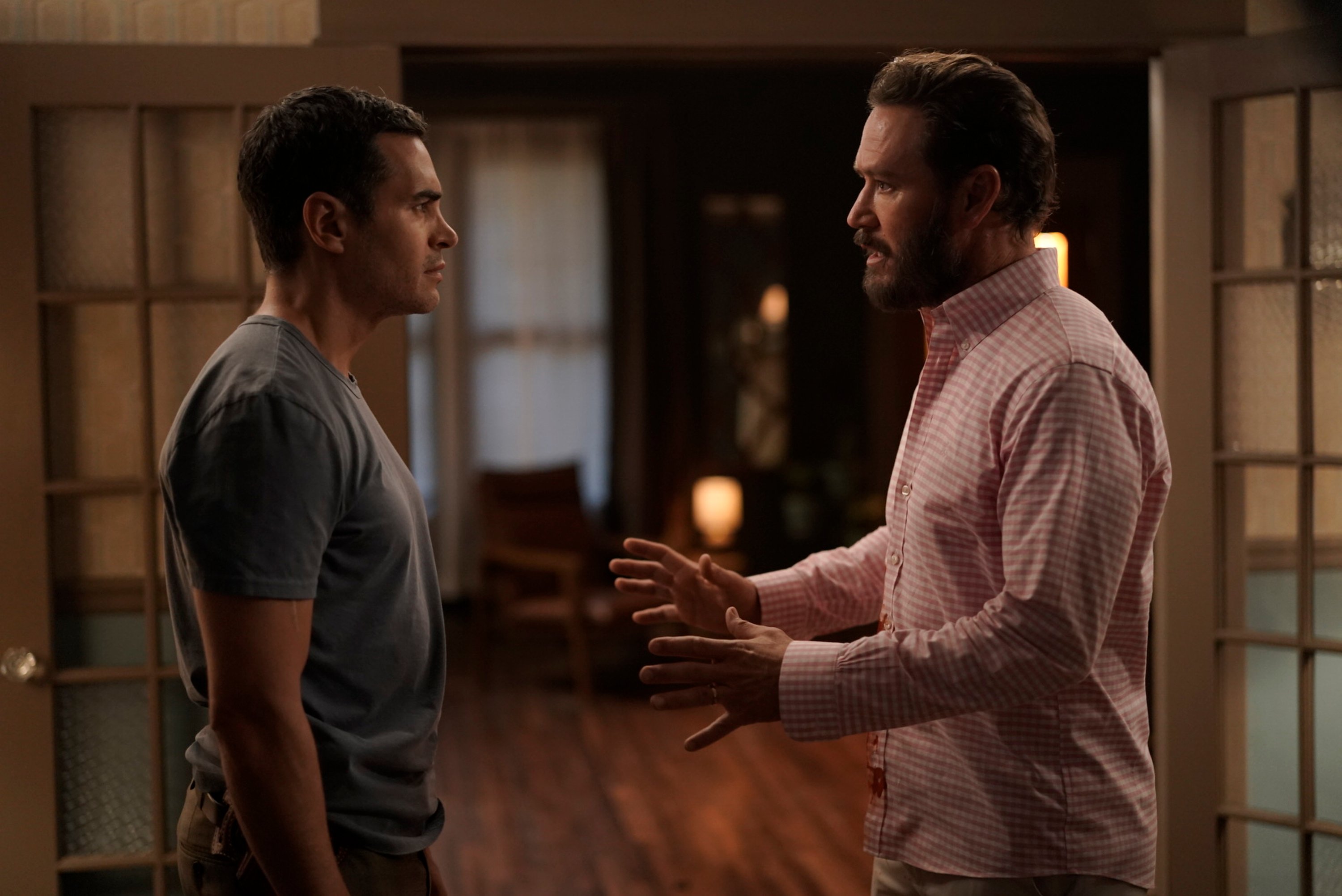 Ramón Rodríguez as Will Trent and Mark-Paul Gosselaar as Paul Campano in 'Will Trent' Season 1 Episode 2, 'I'm a Pretty Observant Guy.' Will wears a dark gray shirt. Paul wears a light pink and white checkered button-up shirt.