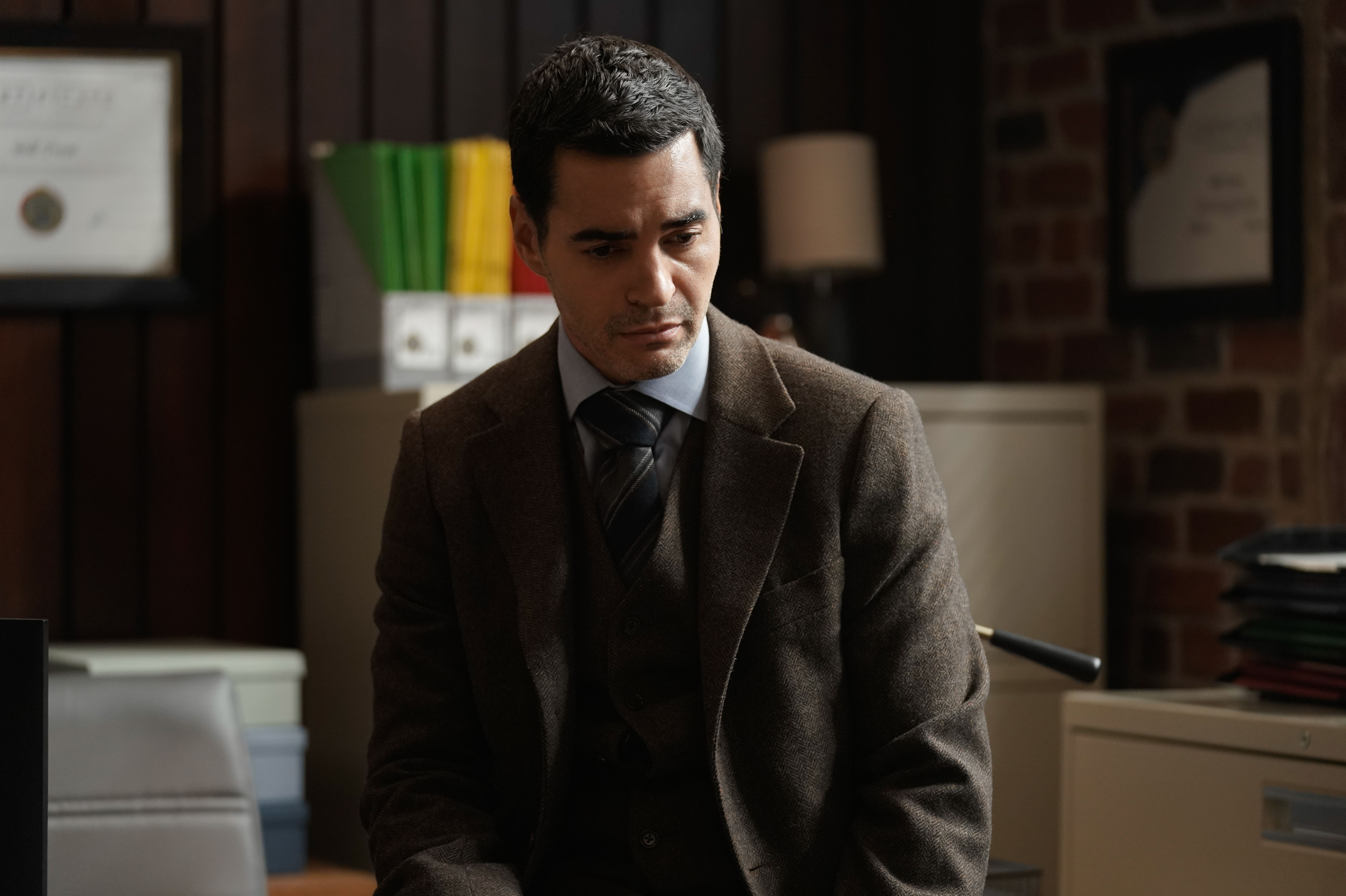 Ramón Rodríguez, in character as Will Trent in 'Will Trent' Season 1 Episode 5, wears a gray three-piece suit over a light blue button-up shirt and black and gray striped tie.
