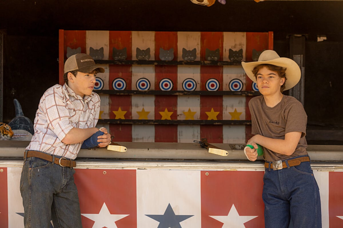 In Yellowstone, Brecken Merrill and Finn Little's characters Tate and Carter stand in front of a shooting game at the fair.