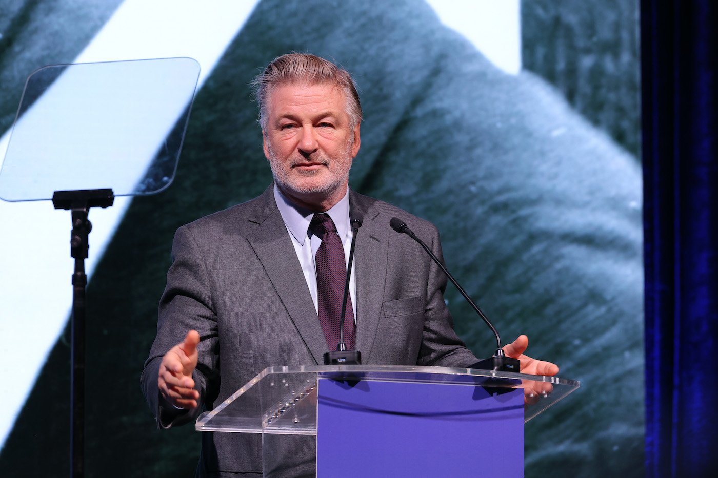 Alec Baldwin speaks at a charity event and stands at a podium 