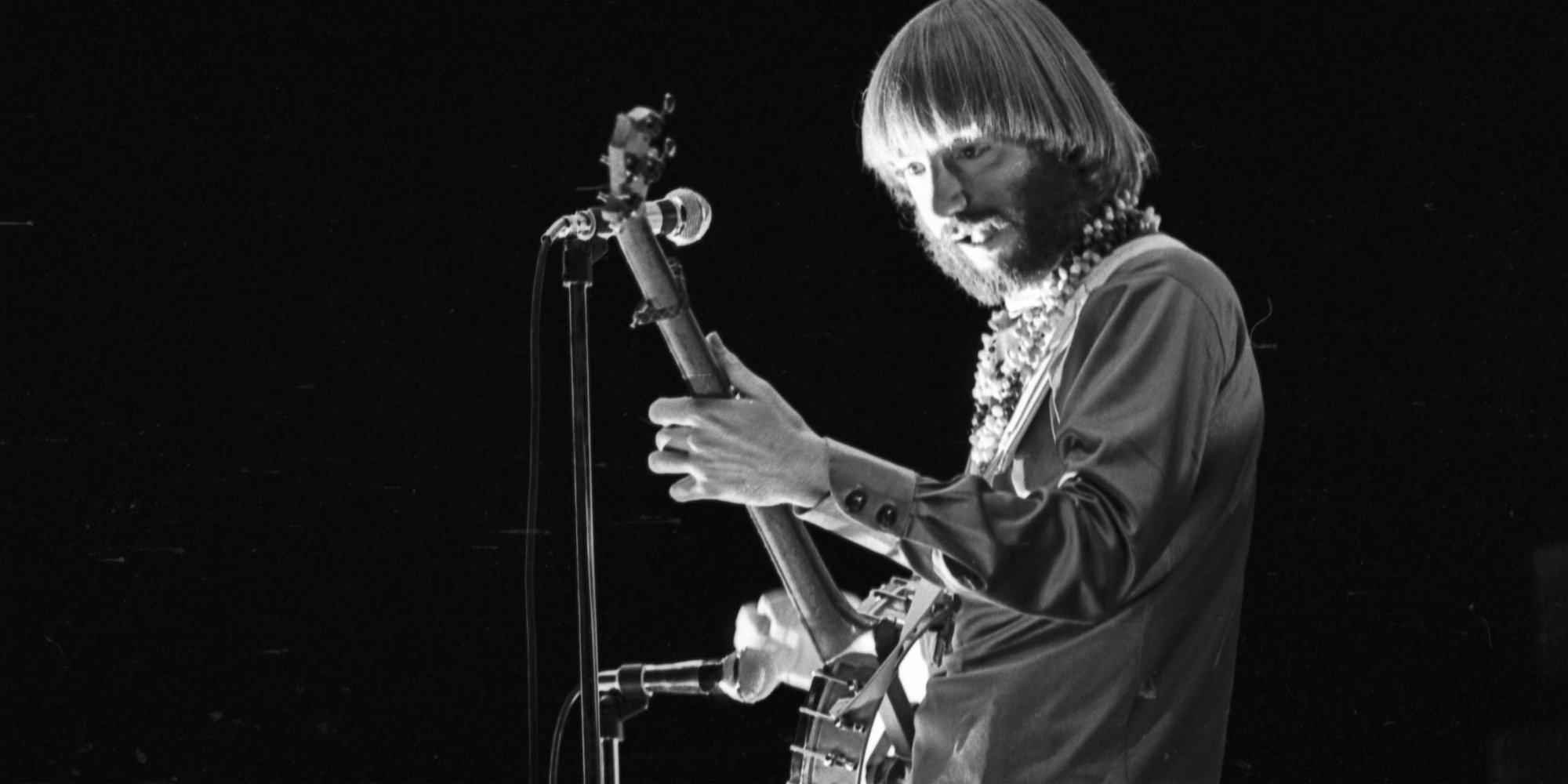 A black and white image of Peter Tork playing guitar.