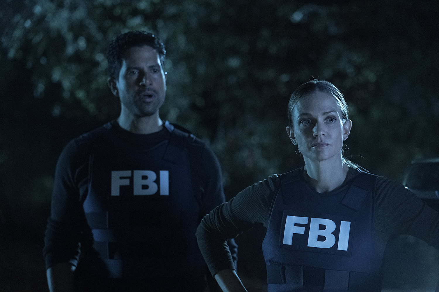 Criminal Minds: Evolution stars Adam Rodriguez as Luke Alvez and A.J. Cook as JJ wearing FBI vests in a dark forest.