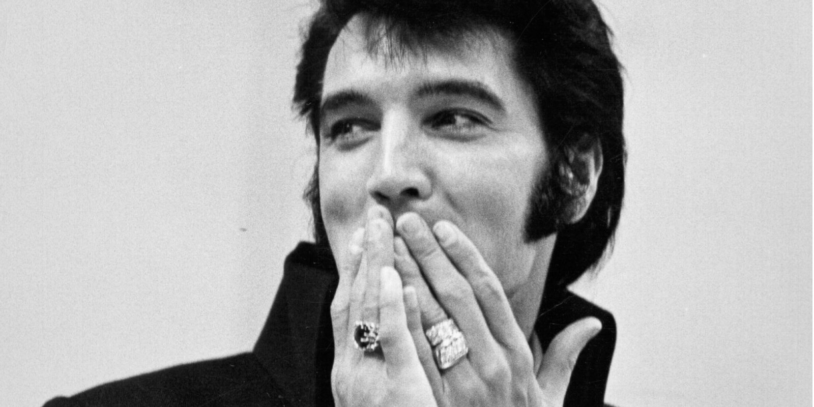Elvis Presley holds his hands in front of his mouth in a black and white photo taken in 1969,