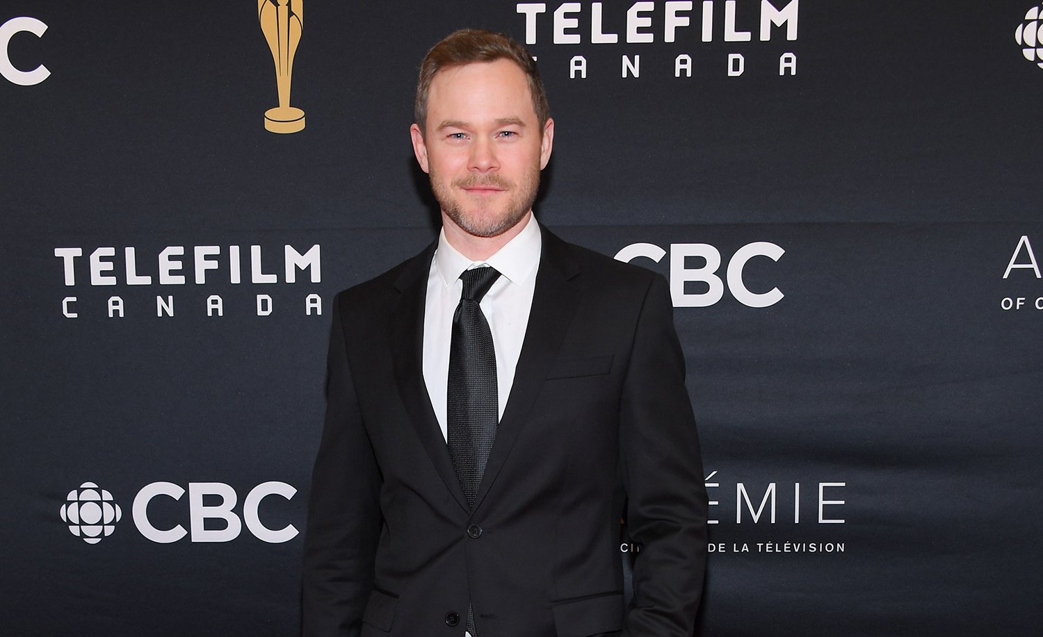 Ginny & Georgia Season 2 Austin's dad Gil actor Aaron Ashmore smiles in a black suit at a red carpet event for the 2019 Canadian Screen Awards Broadcast Gala