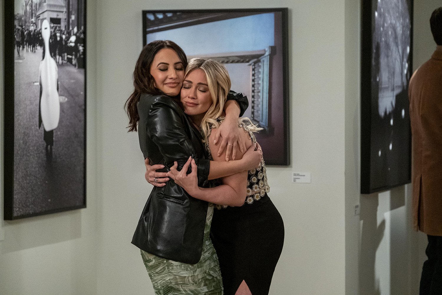 How I Met Your Father Season 1: Francia Raisa as Valentina and Hilary Duff as Sophie embracing in a hug at an art gallery