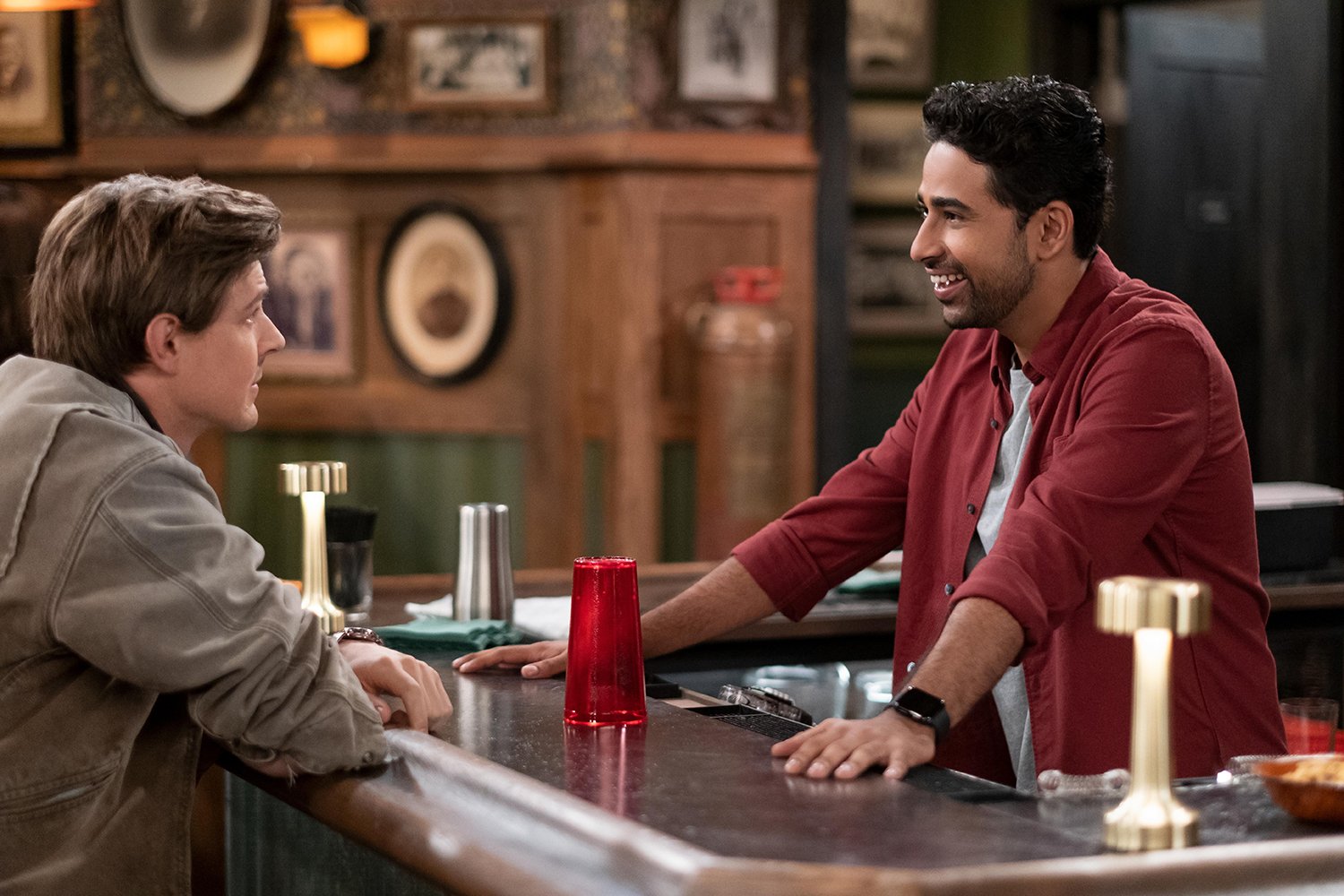 How I Met Your Father Season 2: Chris Lowell as Jesse and Suraj Sharma as Sid chatting on opposite sides of a bar counter.