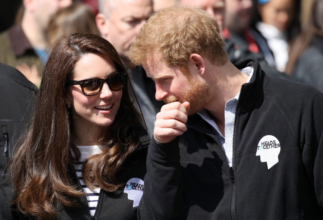 Kate Middleton sits next to Prince Harry and smiles.