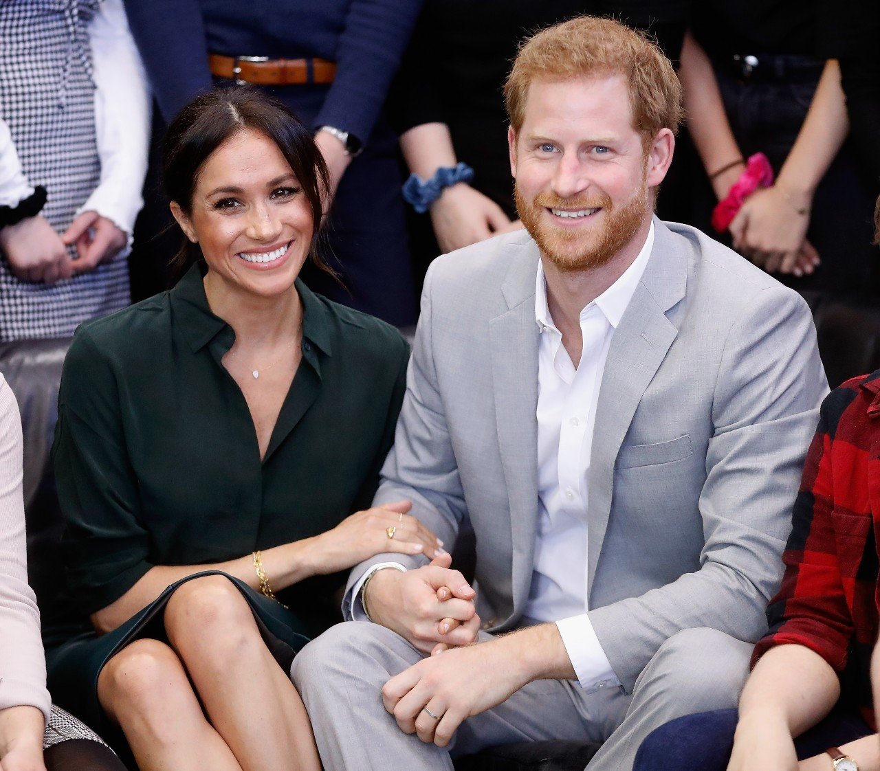 Meghan Markle and Prince Harry sit next to each other and smile.