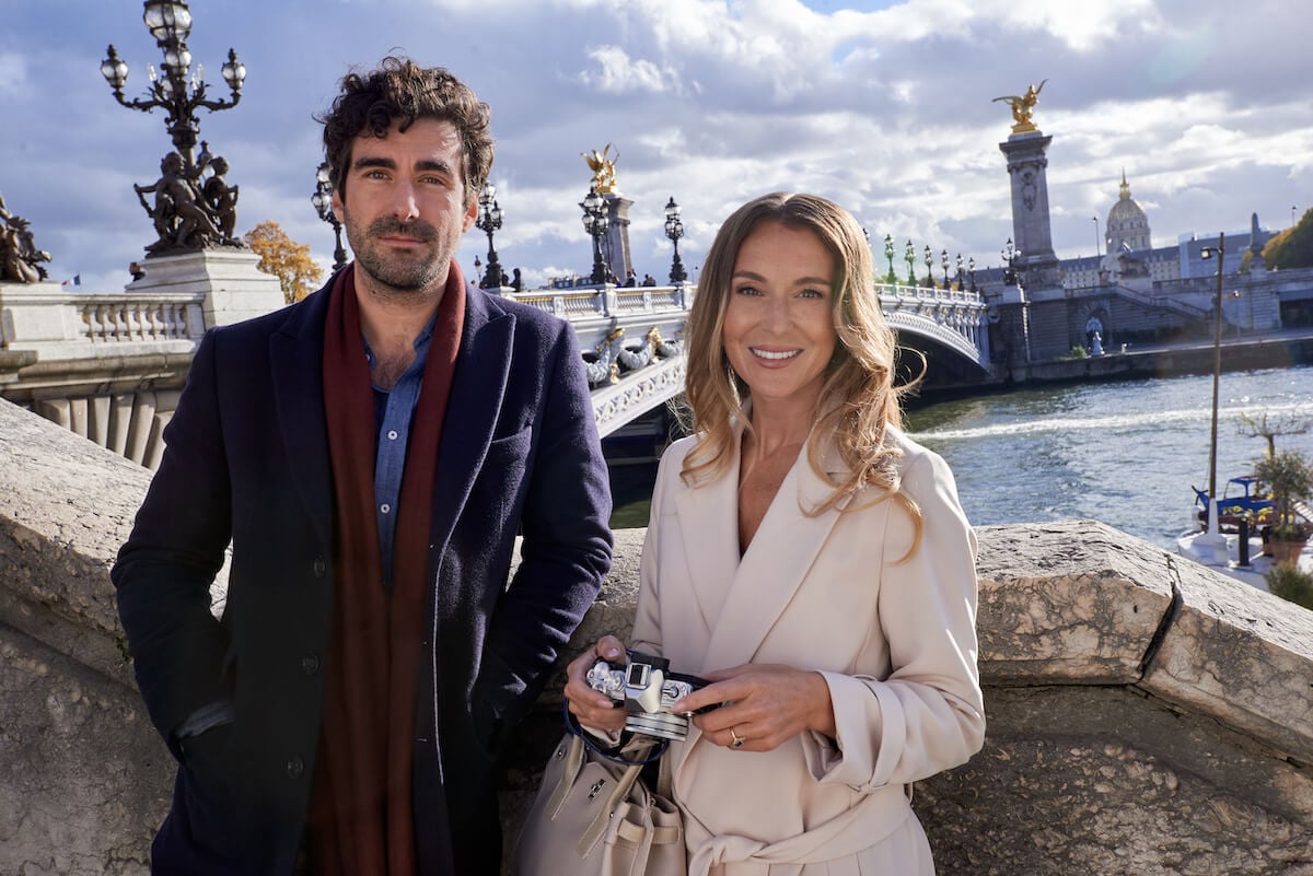 Nicholas Bishop and Alexa PenaVega standing in front of the Alexander III bridge in the Hallmark movie 'A Paris Proposal'