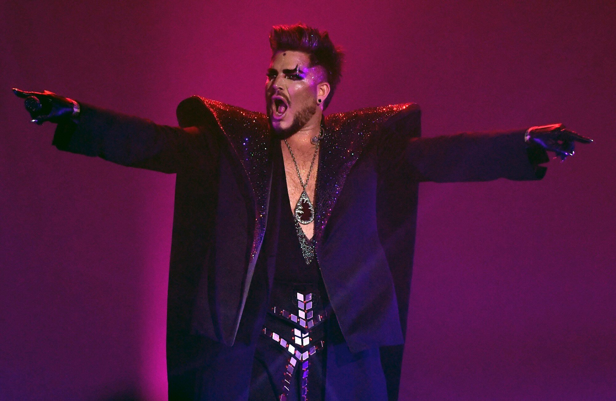Adam Lambert performs on stage wearing a long black coat