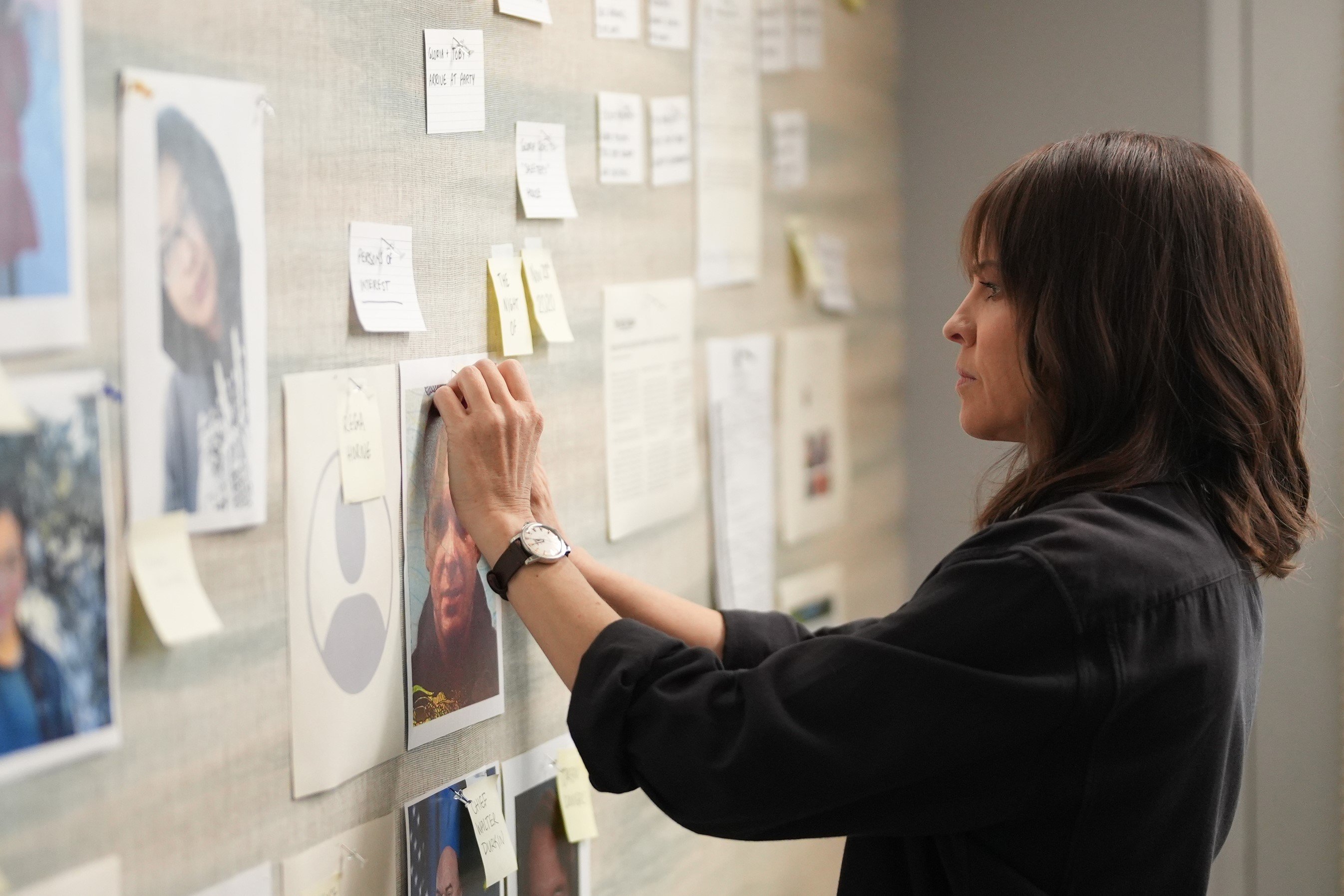 Hilary Swank as Eileen Fitzgerald, who appears in 'Alaska Daily' Episode 7 on ABC, wears a black button-up shirt while pinning a picture to a crime board.