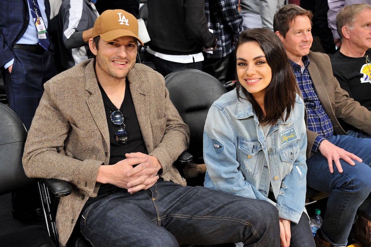 Ashton Kutcher and Mila Kunis smile together at a basketball game.