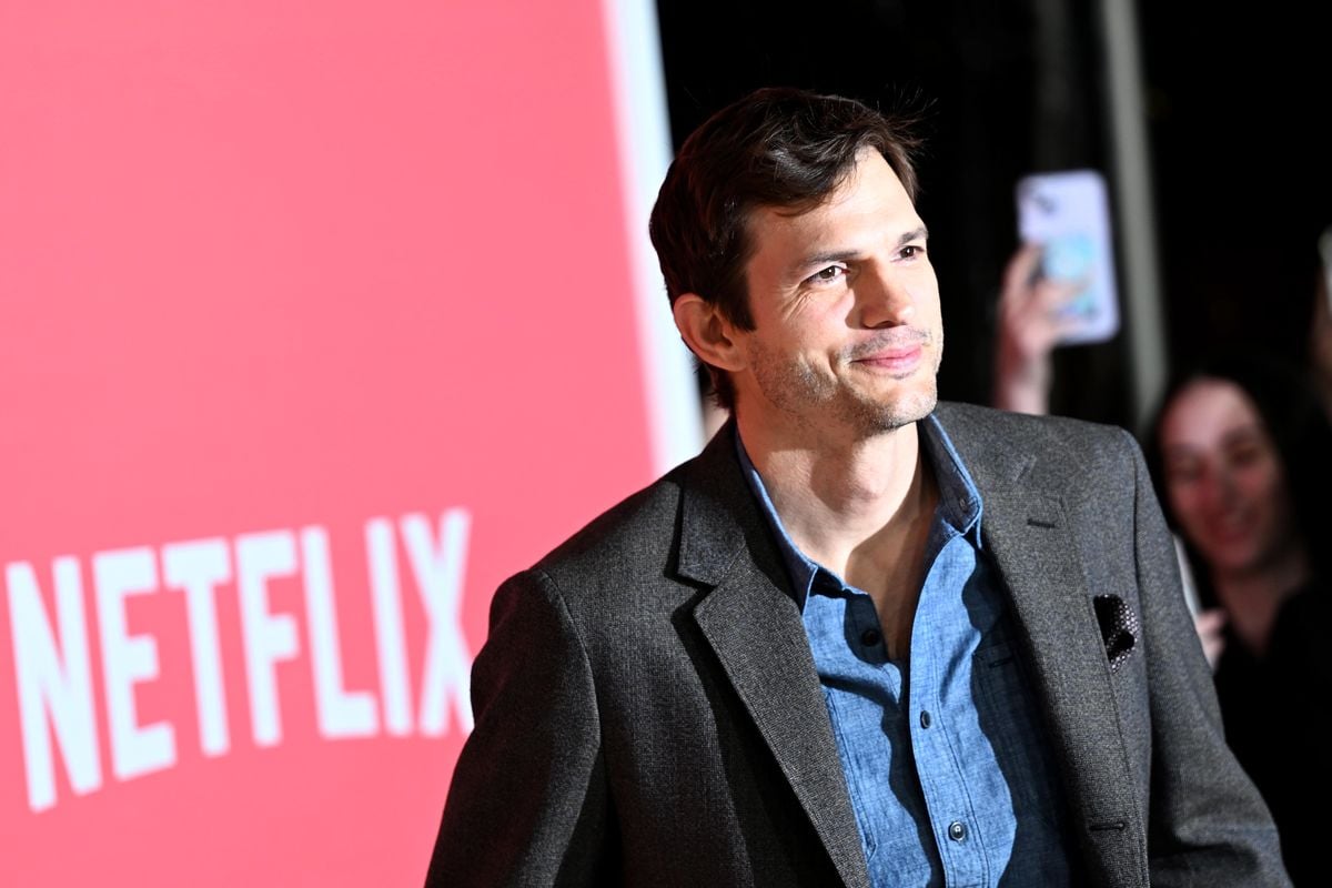 Ashton Kutcher poses for photos in front of a red backdrop with the Netflix logo.