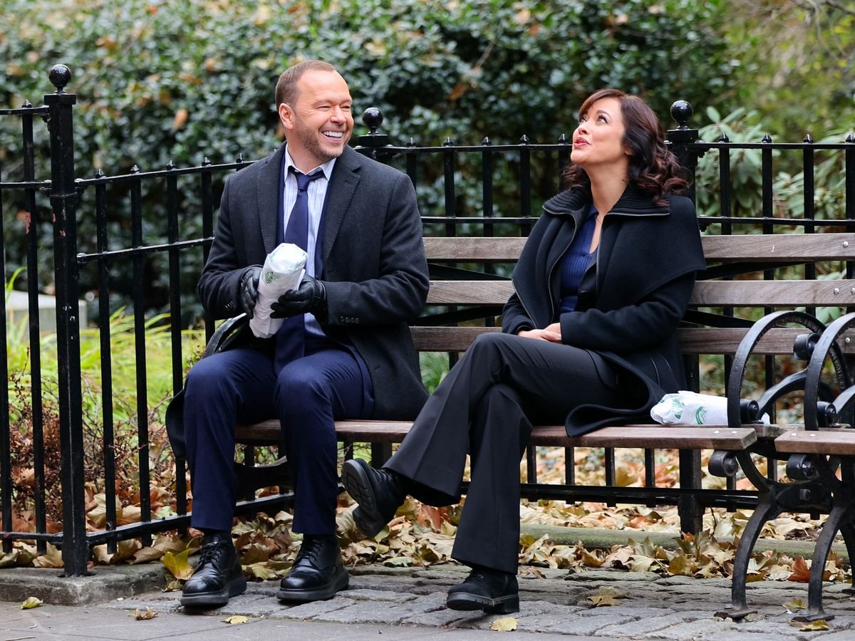 Donnie Wahlberg and Marisa Ramirez sit on a park bench during a shoot for "Blue Bloods"