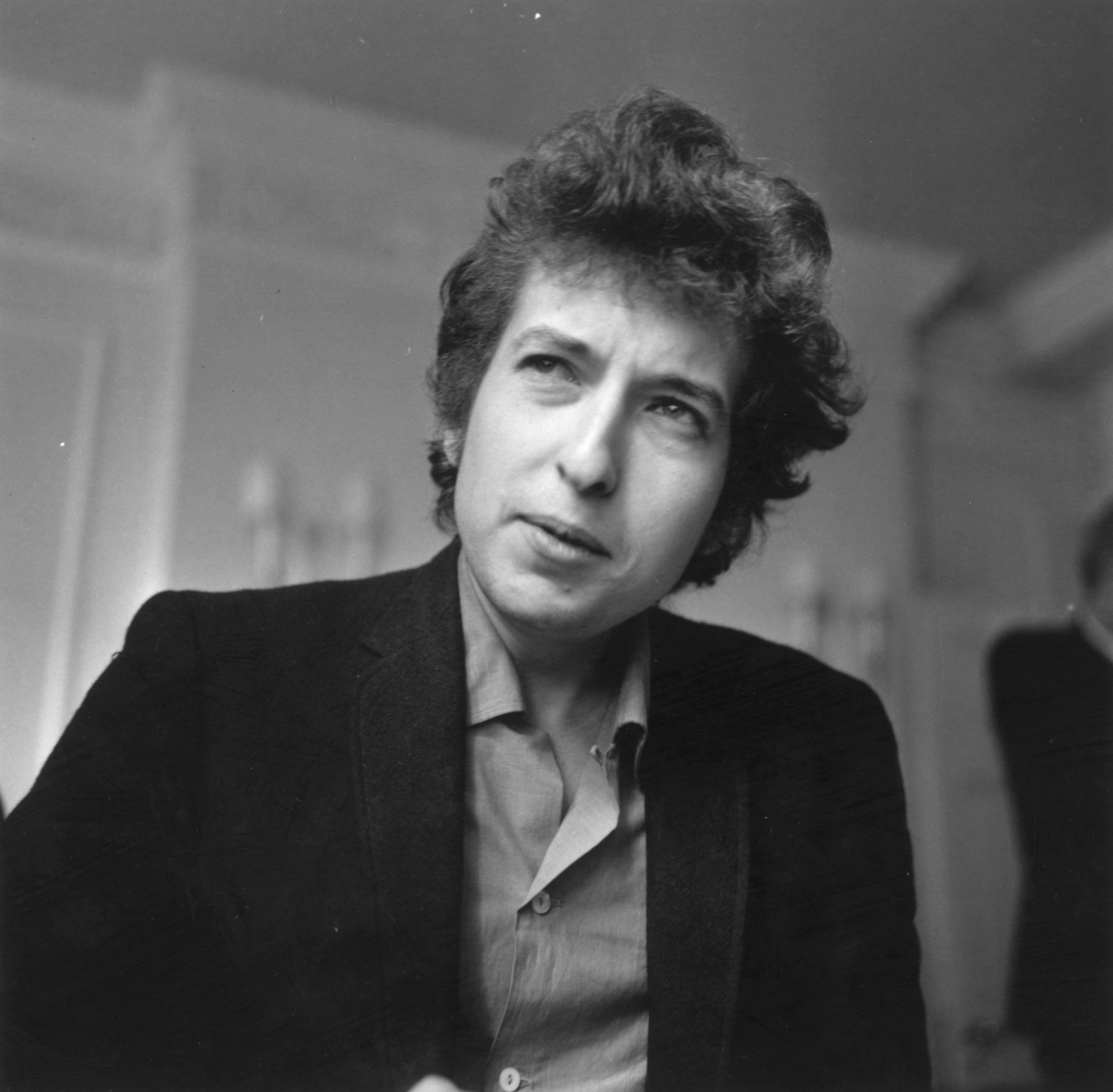 A black and white picture of Bob Dylan wearing a jacket and button down.