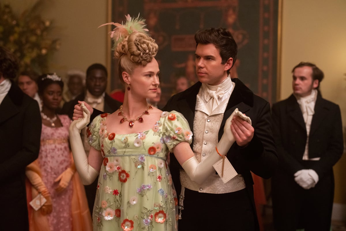 Prior to Bridgerton Season, Cressida and Colin dance at a ball. Cressida wears a floral gown and ruby necklace.