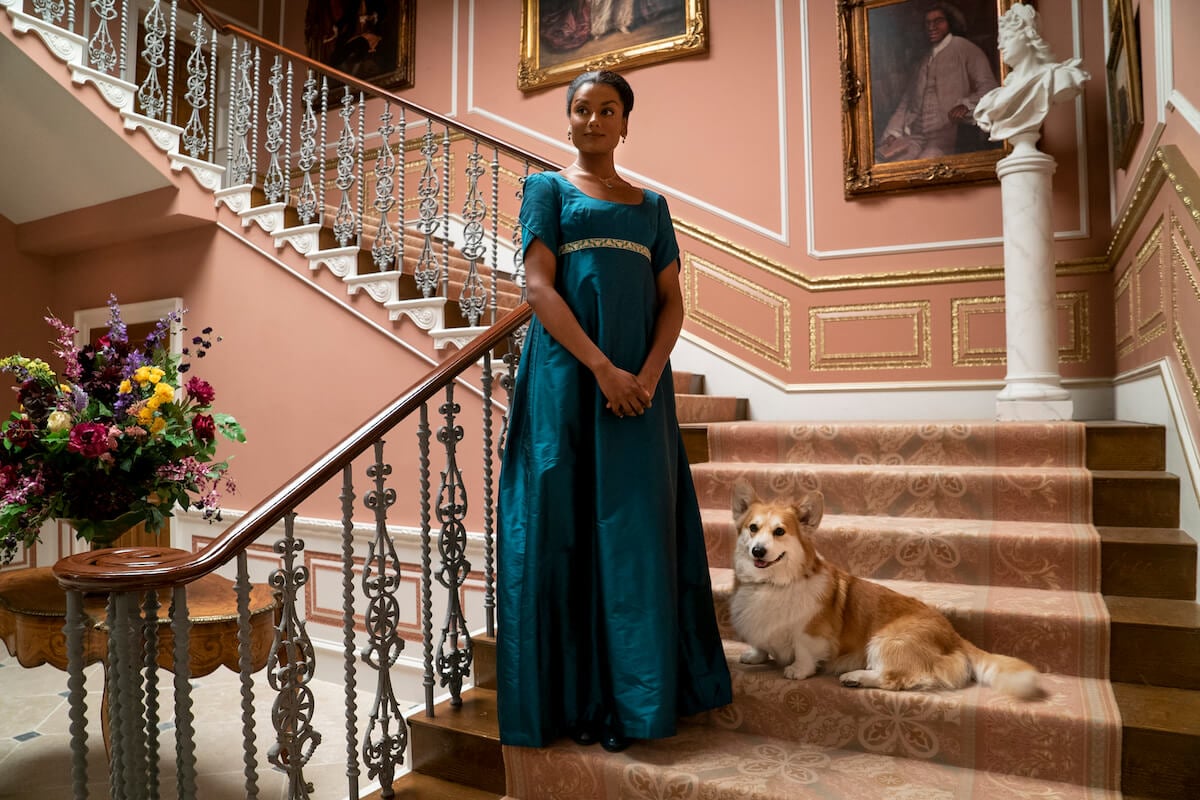 Simone Ashley as Kate Sharma wearing a teal gown and standing on the stairs in 'Bridgerton'