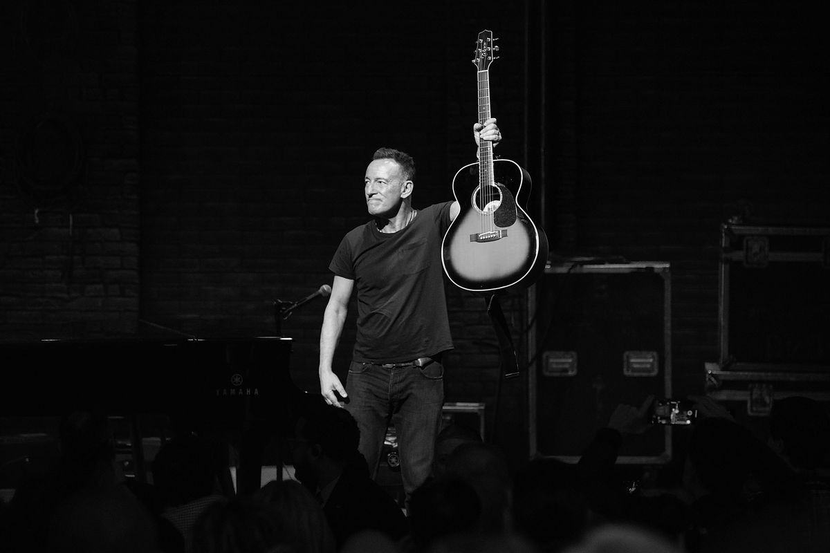 Bruce Springsteen holds a guitar on stage.