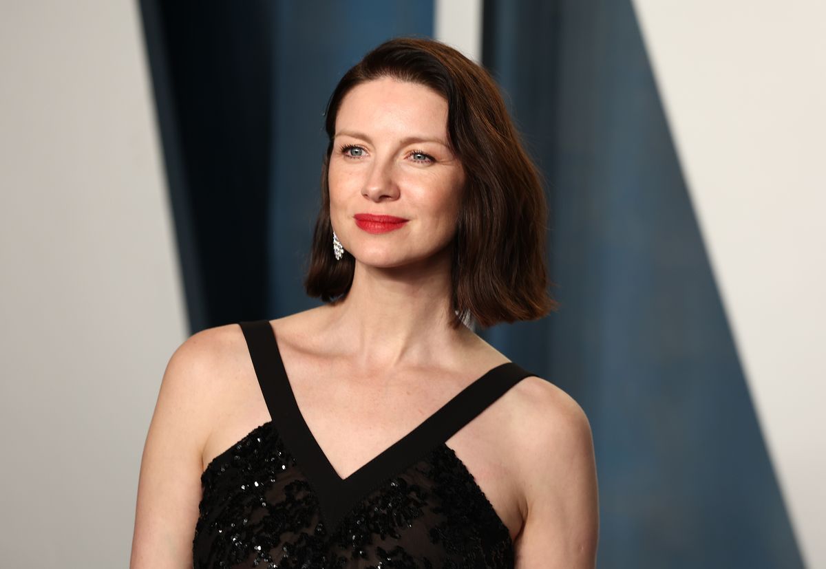 Caitriona Balfe smiles in front of a black and white backdrop.