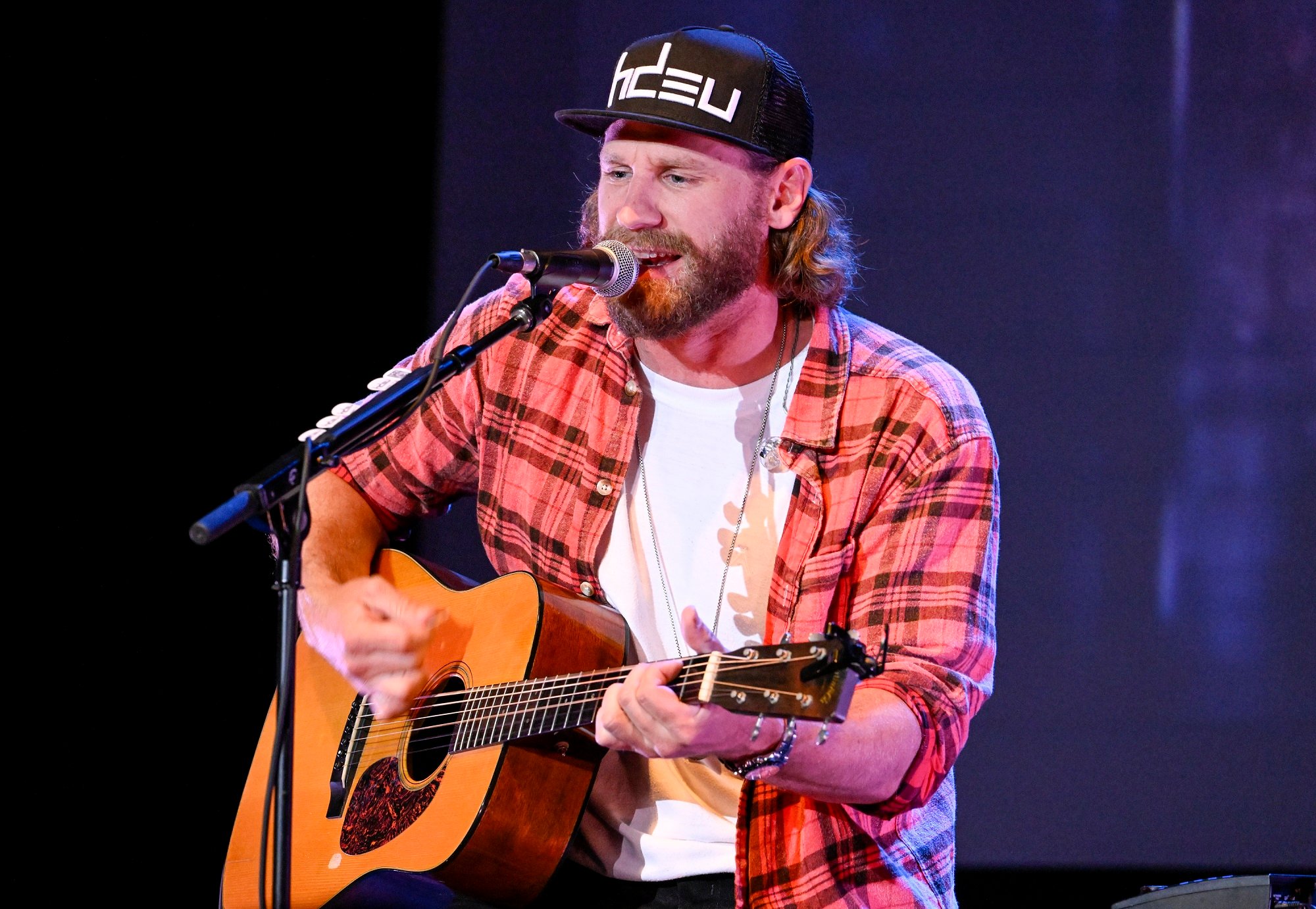 Chase Rice sings into a microphone while playing a guitar on stage