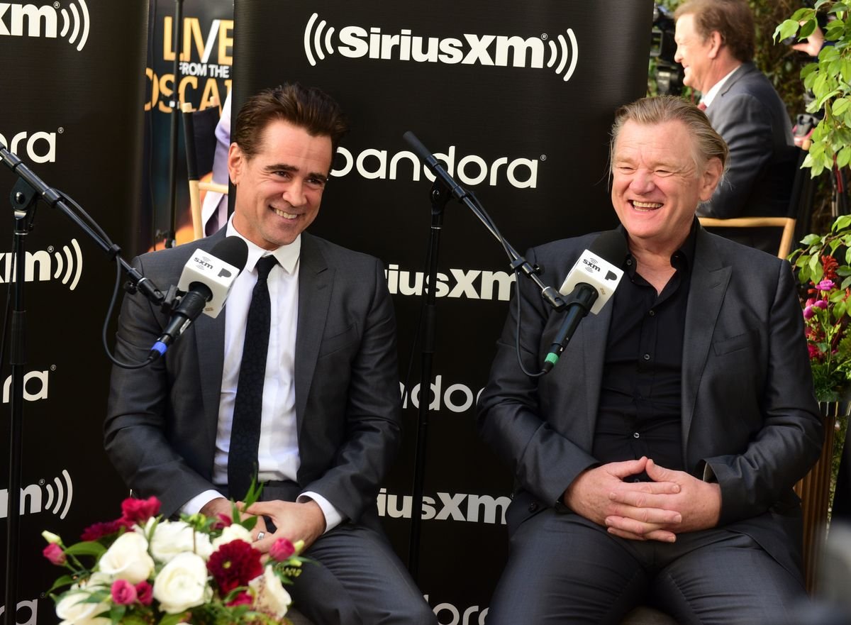 Colin Farrell and Brendan Gleeson speak into microphones against a black backdrop with the Sirius XM logo.