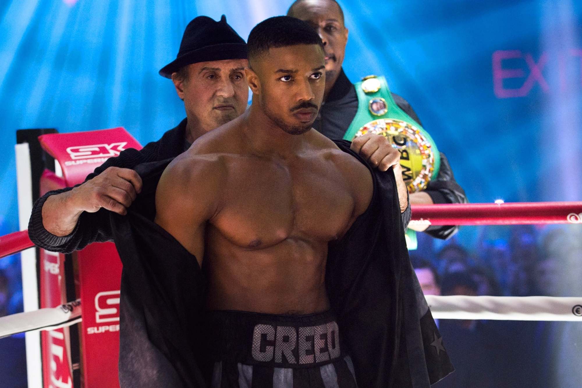 'Creed II' Sylvester Stallone as Rocky and Michael B. Jordan as Adonis Creed. Rocky is standing behind Adonis, taking his jacket off in the boxing ring.