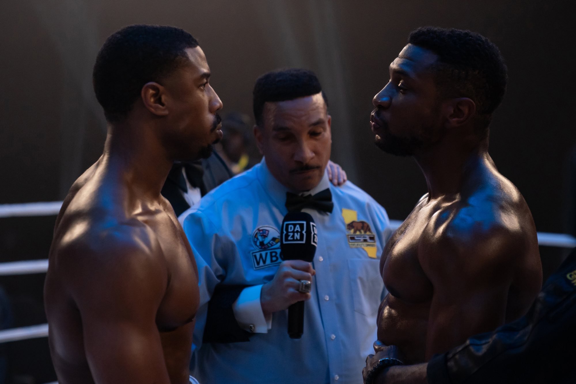 'Creed III' Michael B. Jordan as Adonis Creed and Jonathan Majors as Damian Anderson shirtless in the boxing ring looking at one another with the referee standing in between them