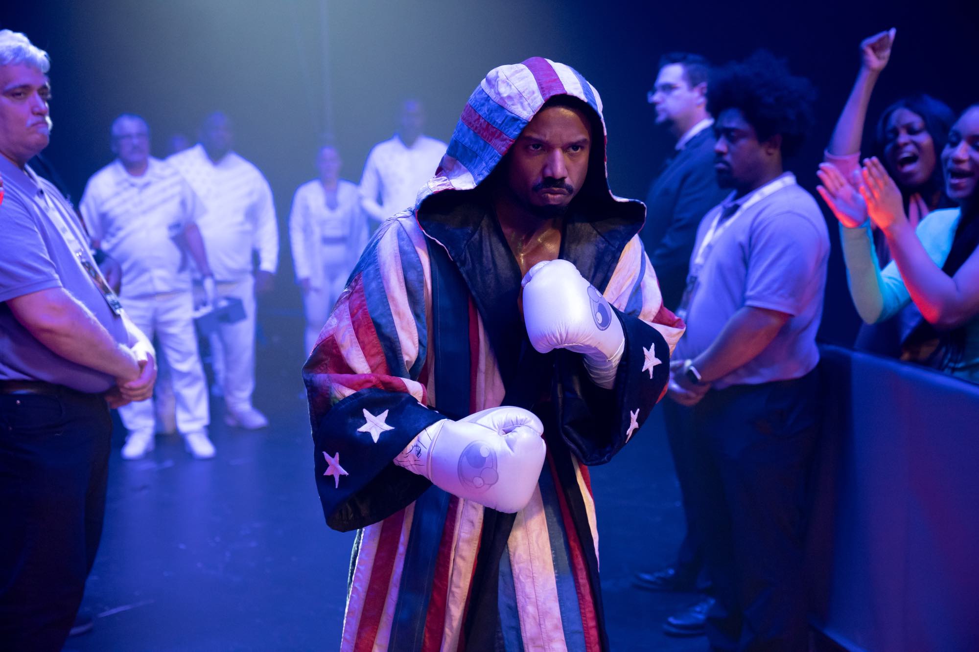 'Creed III' Michael B. Jordan as Adonis Creed wearing an American flag boxing costume hooded and white boxing gloves surrounded by arena-attendants
