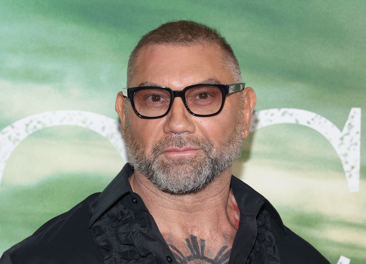 Dave Bautista poses for photos in front of a green backdrop.