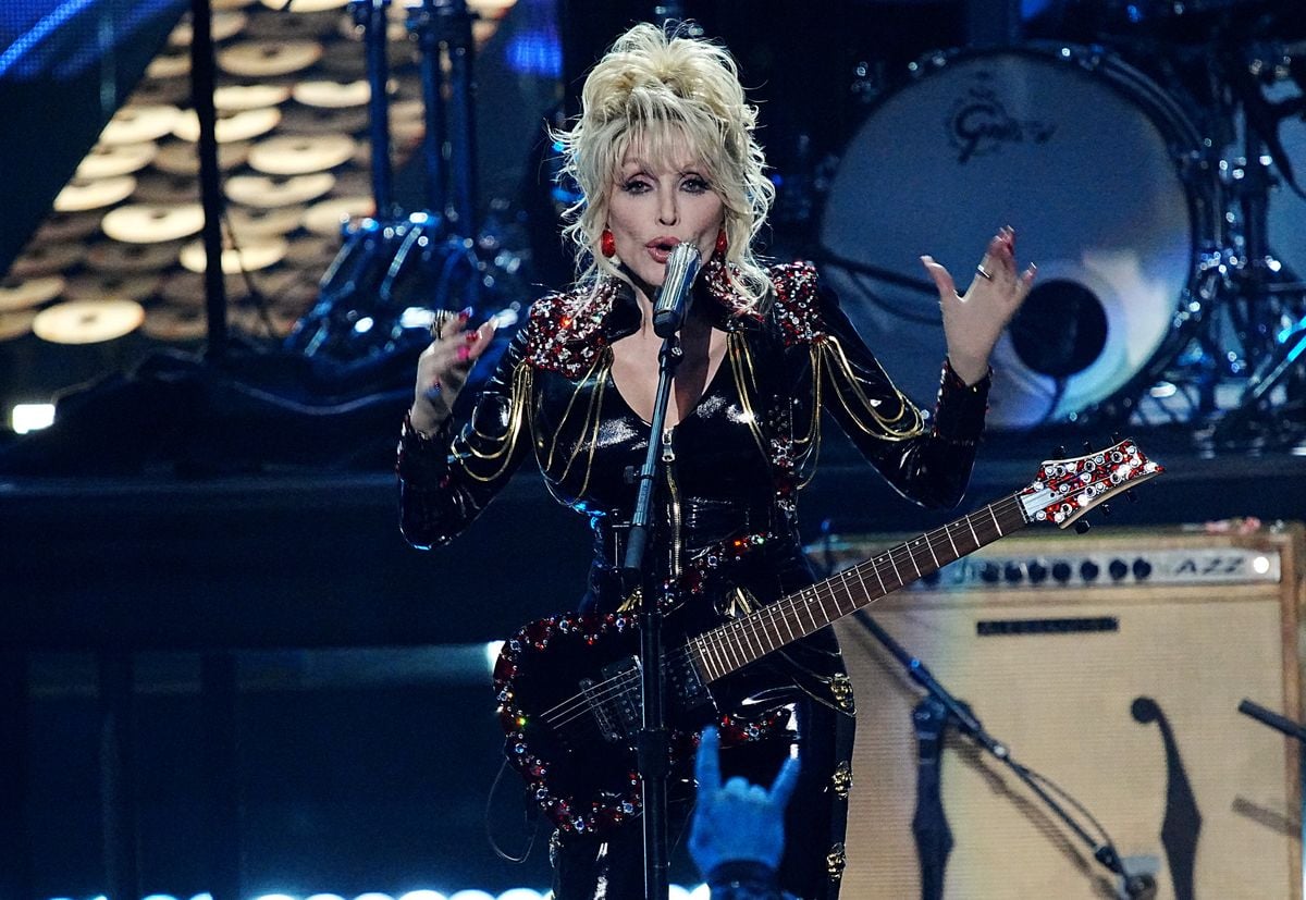 Dolly Parton performs on stage with a guitar.