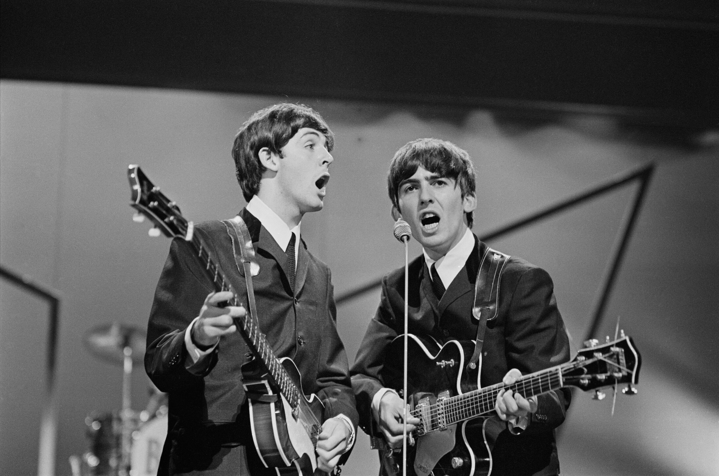 Paul McCartney and George Harrison (1943 - 2001) of the Beatles performing on stage at the London Palladium