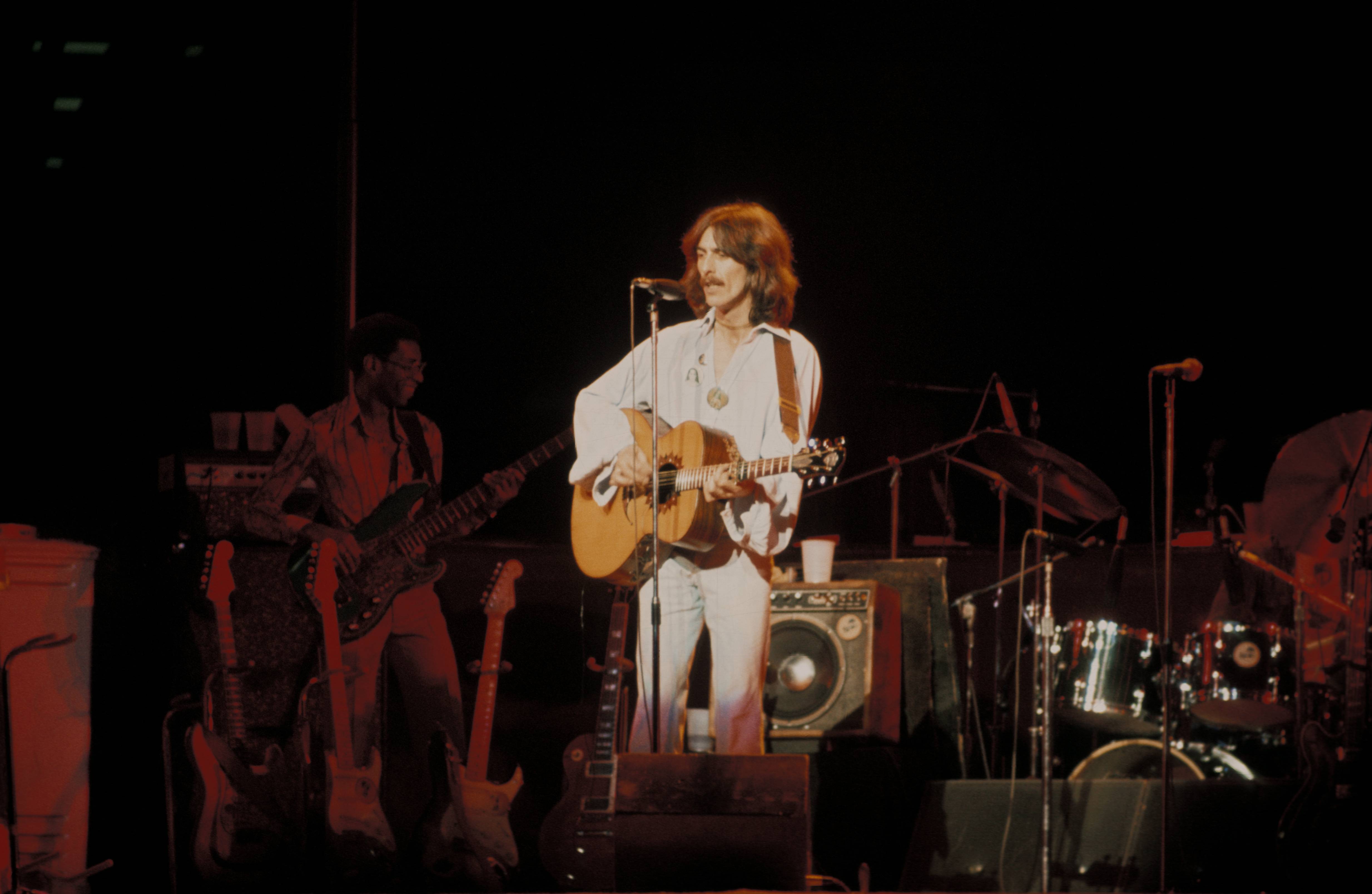 George Harrison performing live onstage on Dark Horse tour, playing acoustic guitar