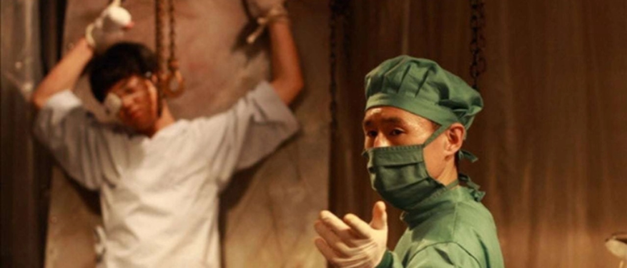 'Grotesque' Hiroaki Kawatsure as Kazuo Kojima and Shigeo Ôsako as The Doctor. Kawatsure is strapped upright with an eye patch and Ôsako is holding his hand out wearing scrubs.