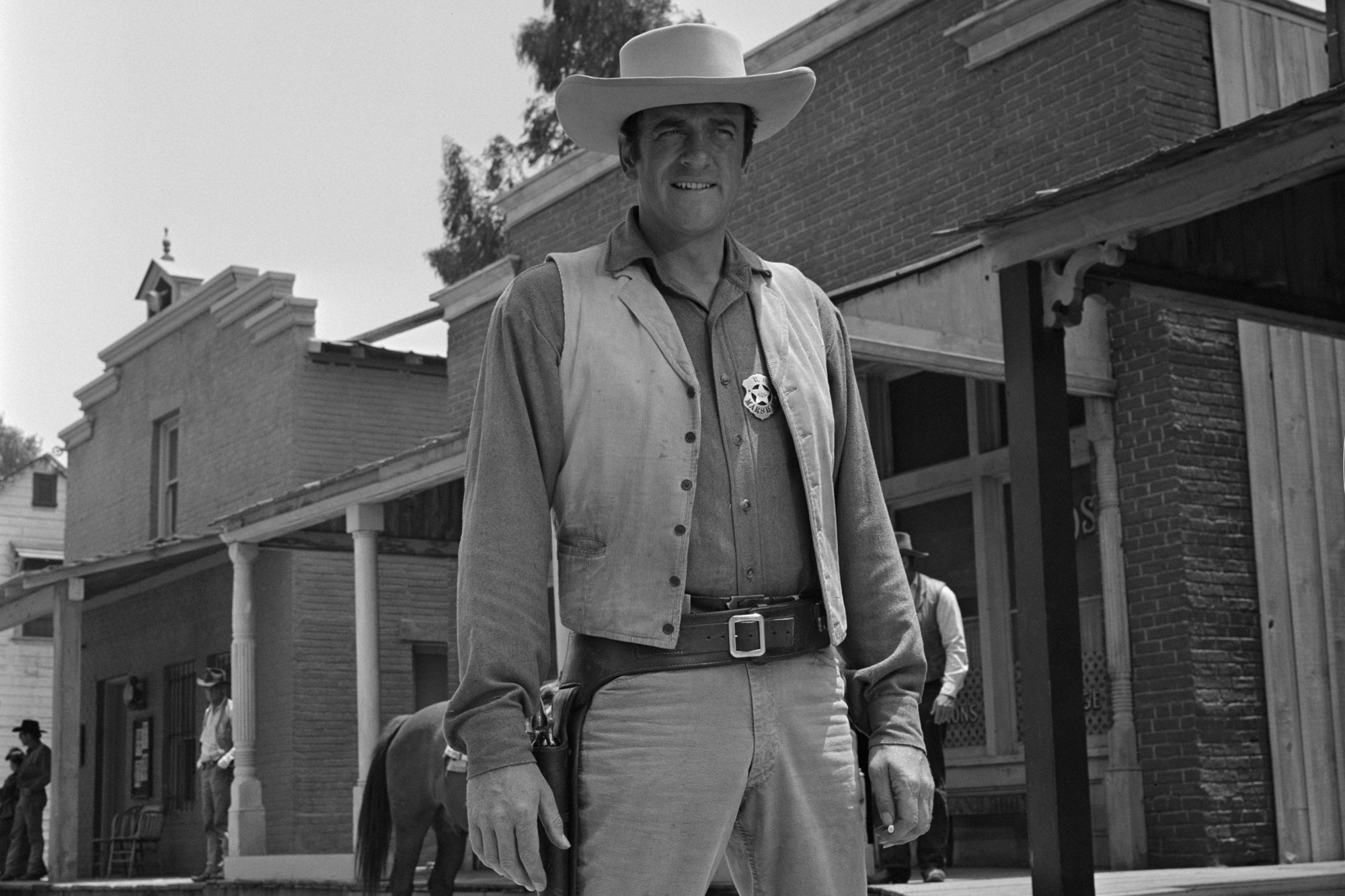 'Gunsmoke' James Arness as U.S. Marshal Matt Dillon in front of Dodge City buildings in a black-and-white picture, wearing a Western costume