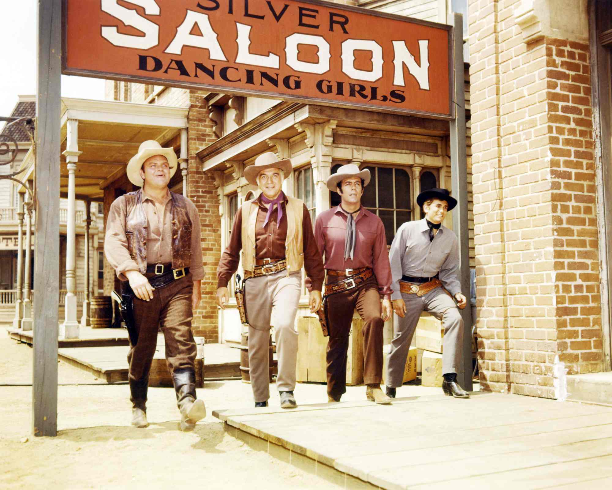 'Gunsmoke' recommendation shows_ 'Bonanza' Dan Blocker as Eric 'Hoss' Cartwright, Lorne Greene as Ben Cartwright, Pernell Roberts as Adam Cartwright, and Michael Landon as Joseph 'Little Joe' Cartwright standing underneath a Saloon sign in Western costumes.