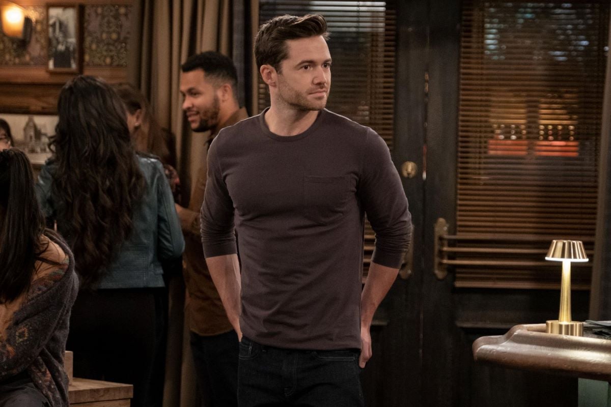 Tom Ainsley, in character as Charlie in 'How I Met Your Father' Season 2 Episode 3, wears a dark brown long-sleeved shirt and dark jeans.