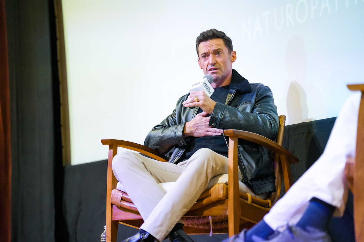 Hugh Jackman speaks into a microphone in front of a blank screen