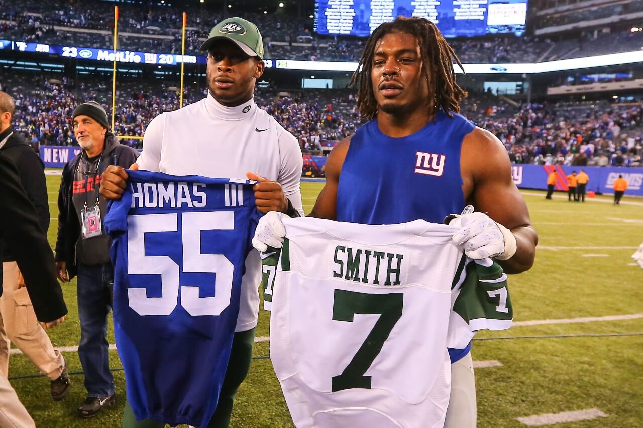 J.T. Thomas III and Geno Smith hold up jerseys for the NY Giants and the NY Jets. 