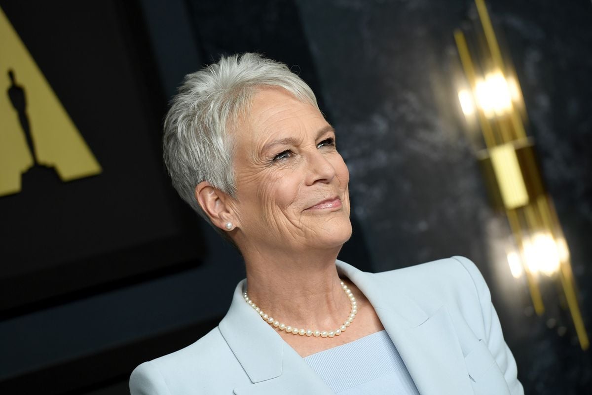 Jamie Lee Curtis poses for photos against a backdrop with an image of the academy awards.
