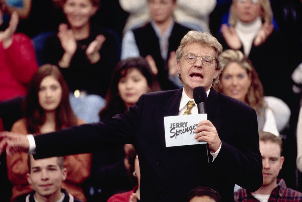 Jerry Springer on his show holding a microphone and a card