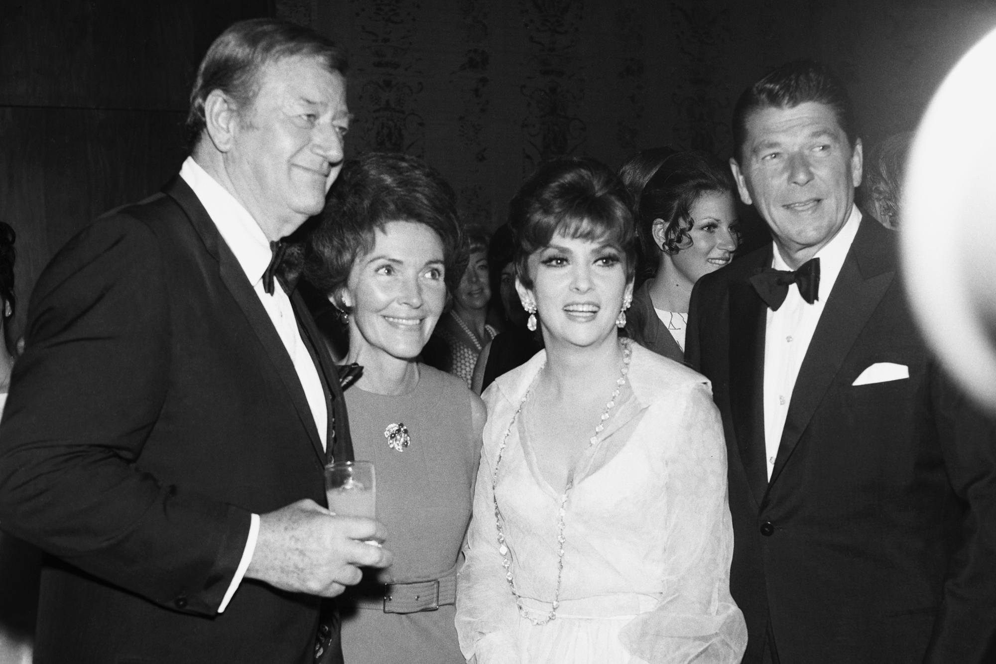 John Wayne, Nancy Reagan, Gina Lollobrigida, and Ronald Reagan in a black-and-white picture in suits and dresses during the National Headliner Awards