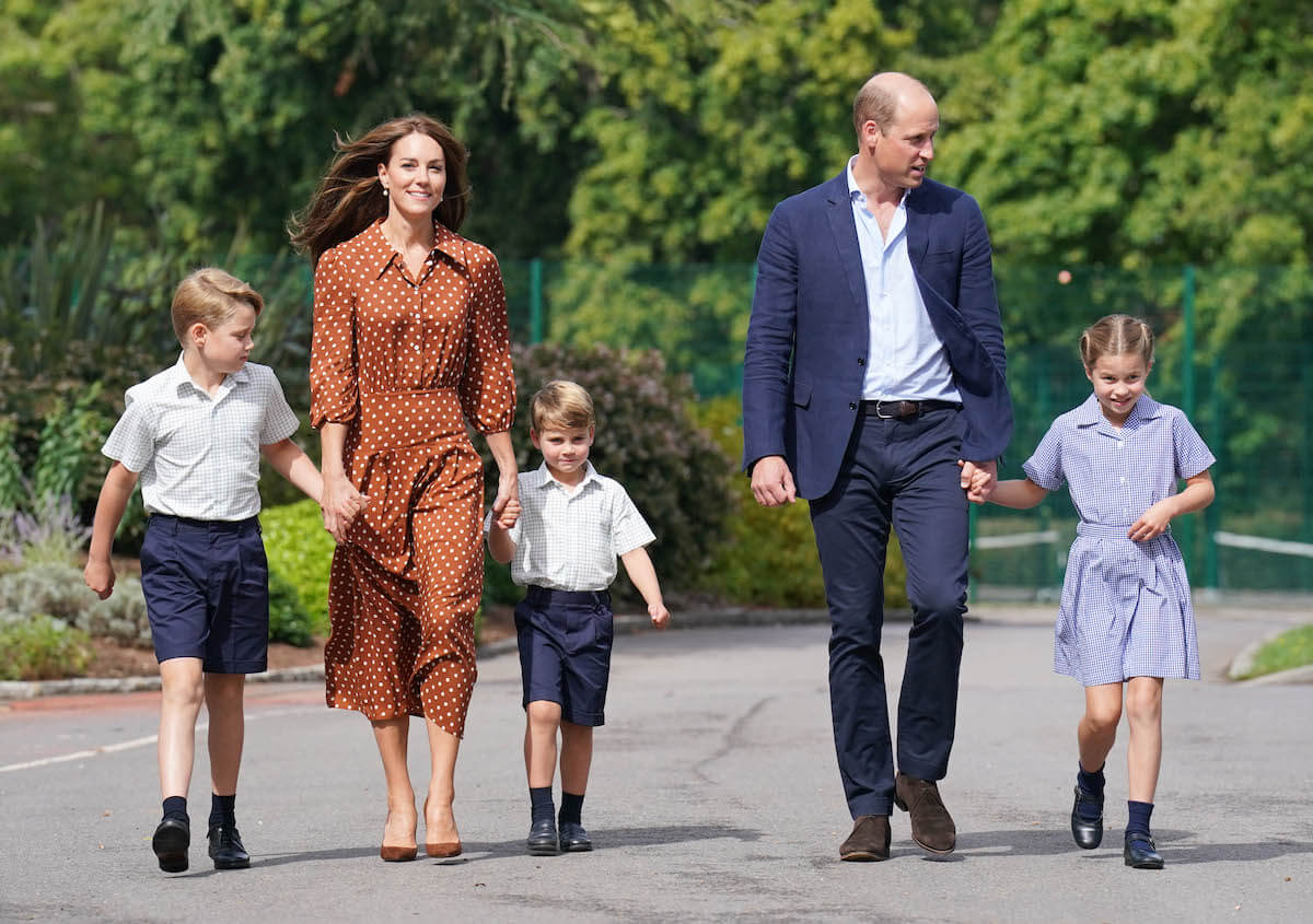 Kate Middleton and Prince William walking outside holding hands with their three kids