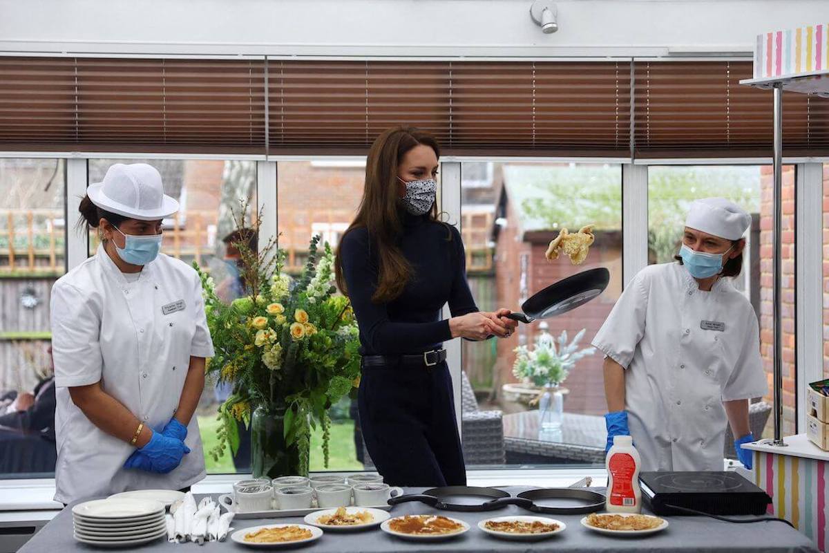 Kate Middleton, who attempted making pancakes, tries to flip a pancake as chefs look on
