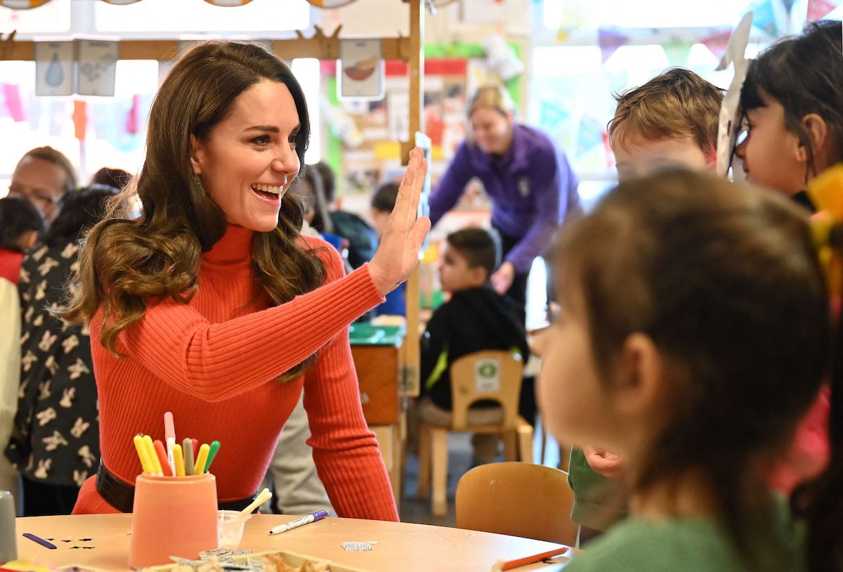Kate Middleton whom some commentators say needs a different approach to Shaping Us and childhood work, high fives a child