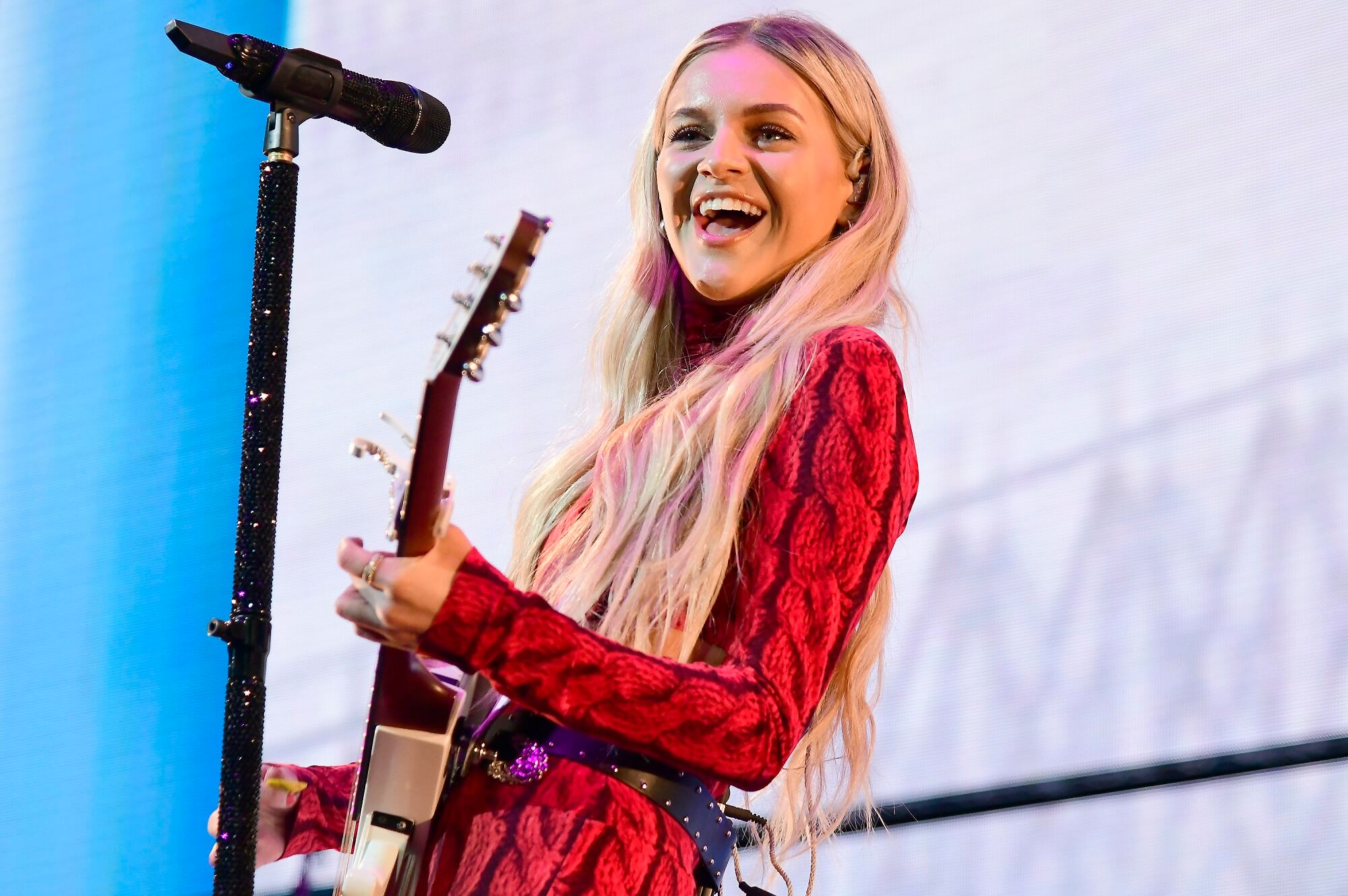 Kelsea Ballerini smiles while performing onstage with a guitar
