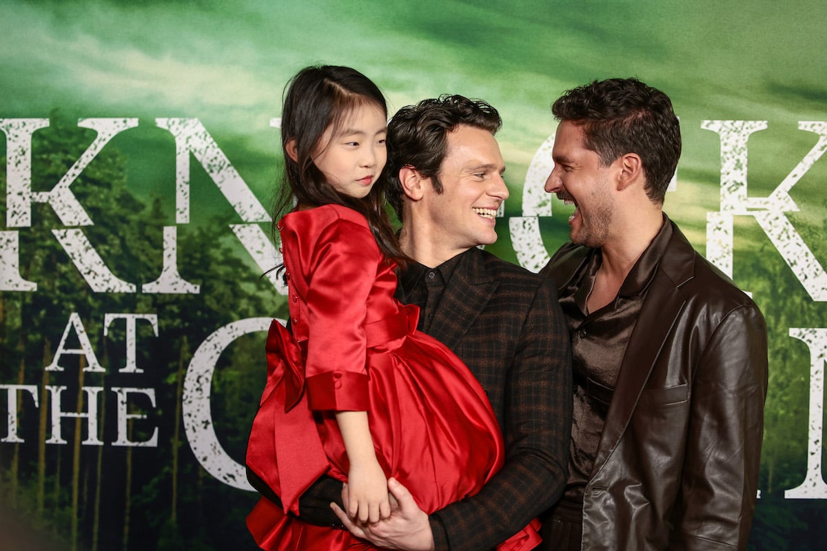 Ben Aldridge and Jonathan Groff hold Kristen Cui in front of a "Knock at the Cabin" backdrop